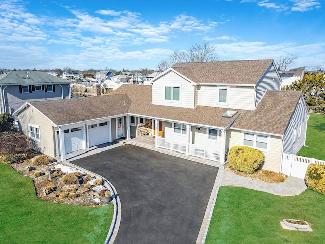 traditional-style house featuring a residential view, roof with shingles, driveway, and a front lawn