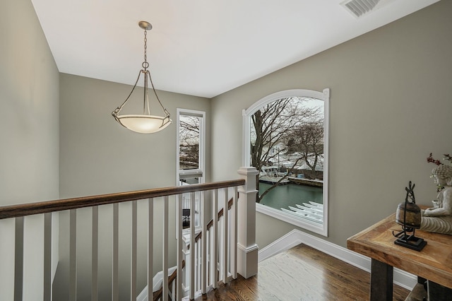 corridor featuring dark wood-type flooring, an upstairs landing, visible vents, and baseboards