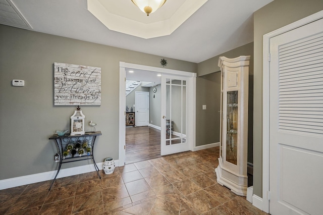 hallway featuring baseboards, visible vents, a raised ceiling, and french doors