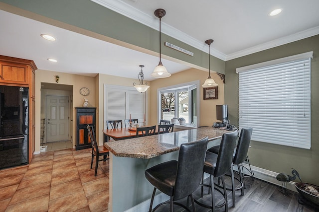 kitchen with a breakfast bar area, brown cabinets, freestanding refrigerator, a peninsula, and pendant lighting