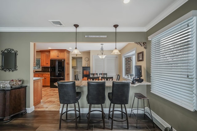 kitchen with visible vents, ornamental molding, decorative light fixtures, freestanding refrigerator, and a kitchen bar