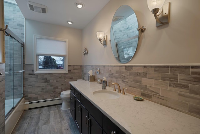 bathroom with visible vents, toilet, baseboard heating, vanity, and tile walls