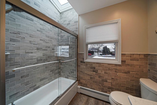 full bath featuring bath / shower combo with glass door, toilet, wood finished floors, a baseboard heating unit, and tile walls