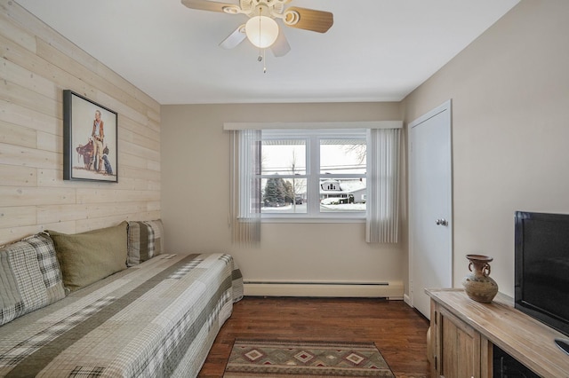 bedroom with a baseboard radiator, wooden walls, a ceiling fan, and dark wood-style flooring