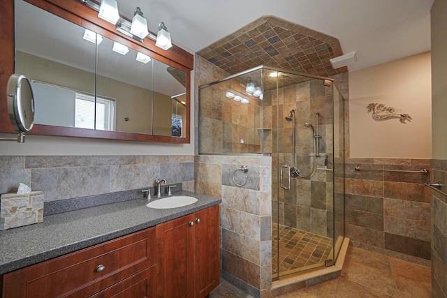 bathroom featuring a stall shower, wainscoting, vanity, and tile walls