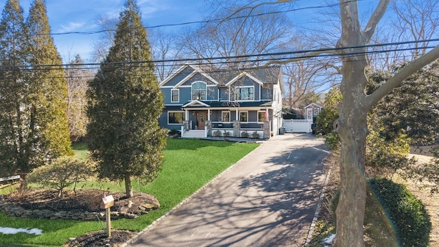 view of front facade featuring covered porch, aphalt driveway, a front lawn, and fence