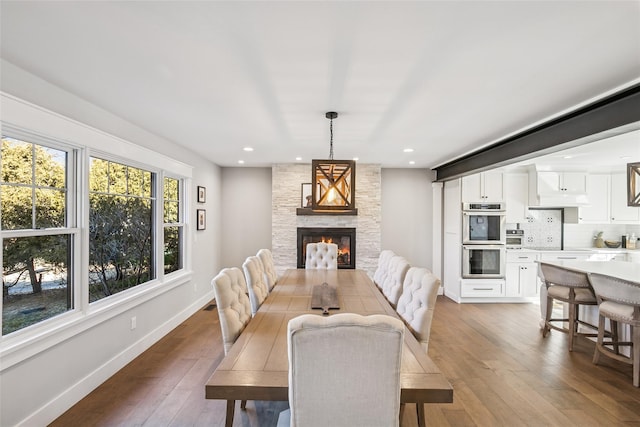 dining area featuring a large fireplace, wood-type flooring, baseboards, and recessed lighting