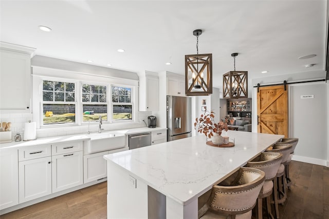 kitchen featuring a barn door, wood finished floors, a kitchen island, appliances with stainless steel finishes, and tasteful backsplash