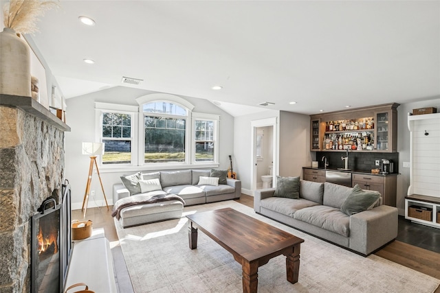 living area with visible vents, wood finished floors, a lit fireplace, wet bar, and vaulted ceiling