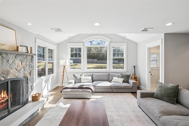 living room with vaulted ceiling, a stone fireplace, wood finished floors, and visible vents