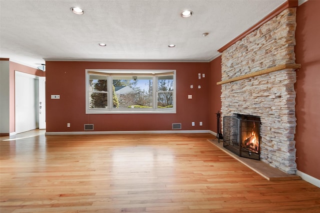 unfurnished living room with a fireplace, visible vents, baseboards, ornamental molding, and light wood finished floors