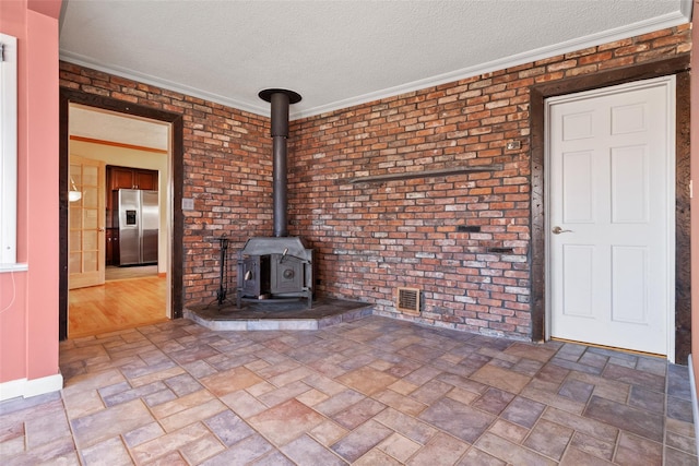 unfurnished living room with a textured ceiling, brick wall, ornamental molding, stone finish flooring, and a wood stove