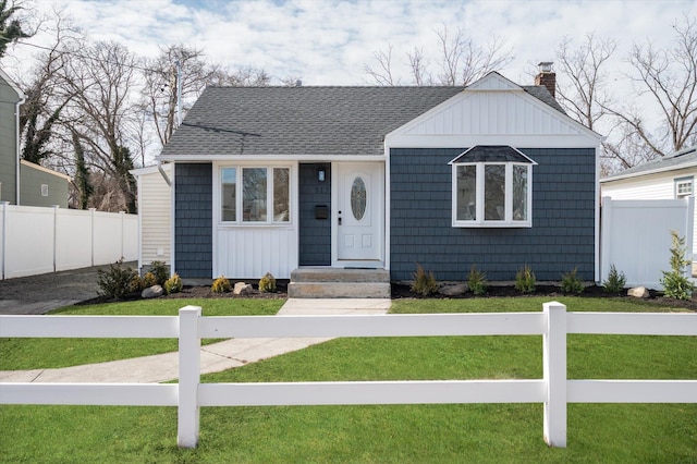 bungalow-style home with roof with shingles, fence, a chimney, and a front lawn