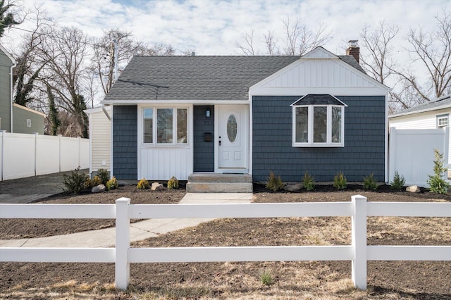 bungalow-style house with a shingled roof, a chimney, and fence