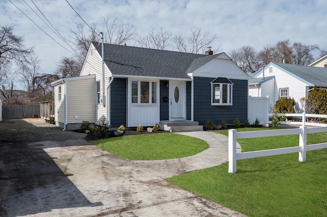 view of front of house featuring a shingled roof, fence, concrete driveway, a chimney, and a front yard