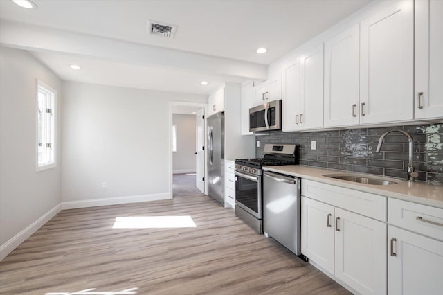 kitchen with a sink, visible vents, light wood-style floors, appliances with stainless steel finishes, and tasteful backsplash