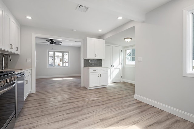 kitchen with light wood finished floors, light countertops, visible vents, decorative backsplash, and a sink