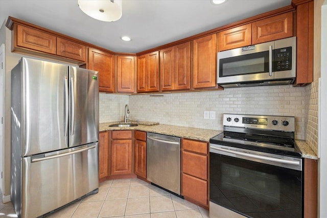 kitchen with appliances with stainless steel finishes, brown cabinetry, light tile patterned flooring, and a sink