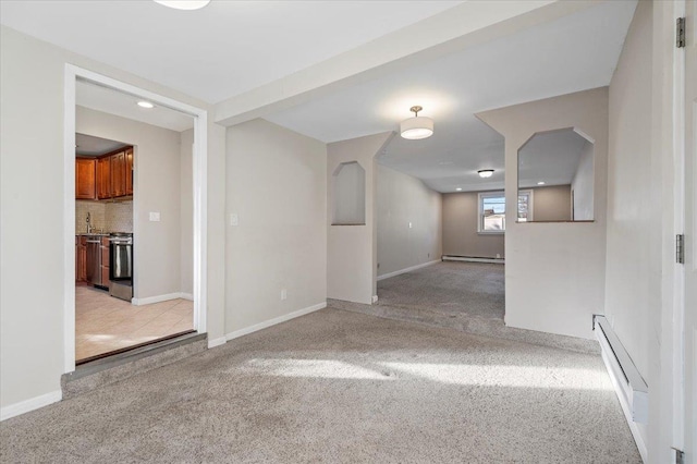 empty room with a baseboard heating unit, light carpet, and baseboards