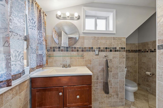 bathroom with lofted ceiling, toilet, vanity, tile walls, and wainscoting