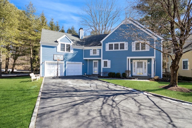 view of front of home featuring a garage, driveway, roof with shingles, a chimney, and a front yard