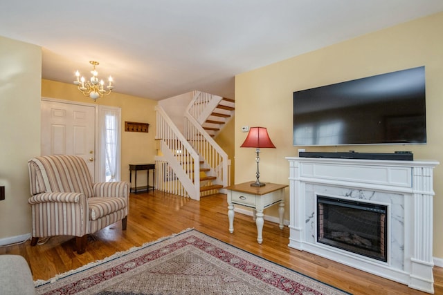 living area with stairway, an inviting chandelier, a high end fireplace, wood finished floors, and baseboards