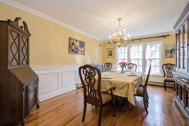 dining space with a baseboard heating unit, a wainscoted wall, wood finished floors, and crown molding