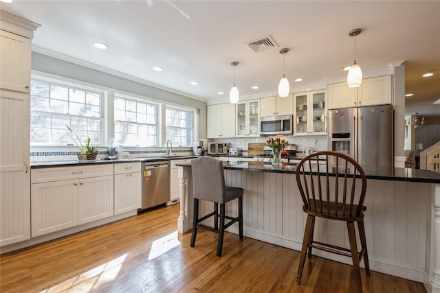 kitchen with visible vents, light wood-style flooring, stainless steel appliances, a kitchen bar, and backsplash