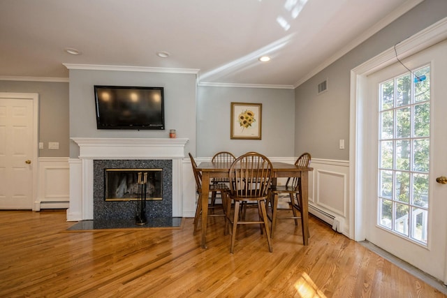 dining area with visible vents, a premium fireplace, baseboard heating, crown molding, and light wood-style floors