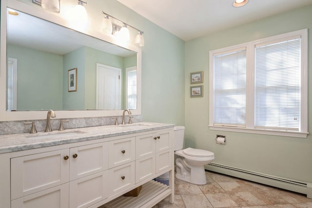 full bath with double vanity, baseboard heating, a sink, and toilet