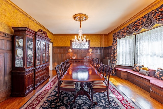 dining room featuring a wainscoted wall, a notable chandelier, wood-type flooring, ornamental molding, and wallpapered walls