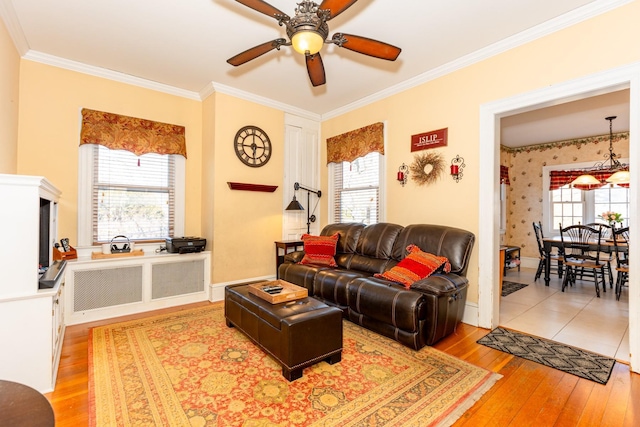 living area with light wood finished floors, ornamental molding, a ceiling fan, baseboards, and wallpapered walls