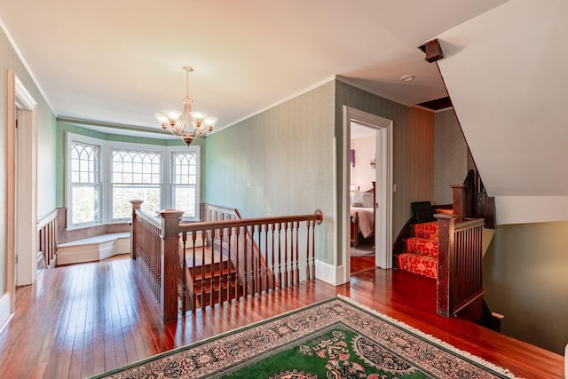 corridor with ornamental molding, hardwood / wood-style flooring, an upstairs landing, and an inviting chandelier