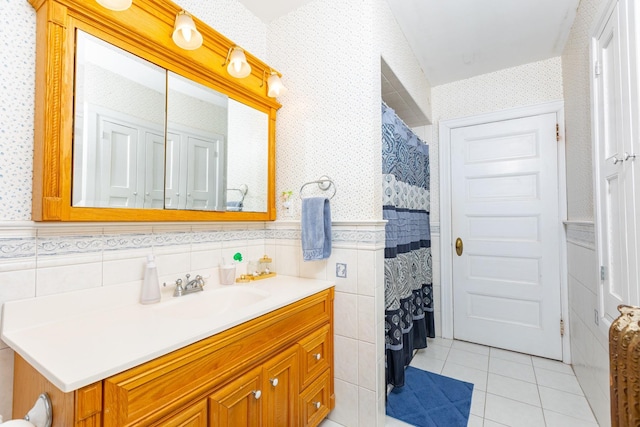 full bathroom featuring wallpapered walls, a wainscoted wall, tile patterned floors, vanity, and tile walls