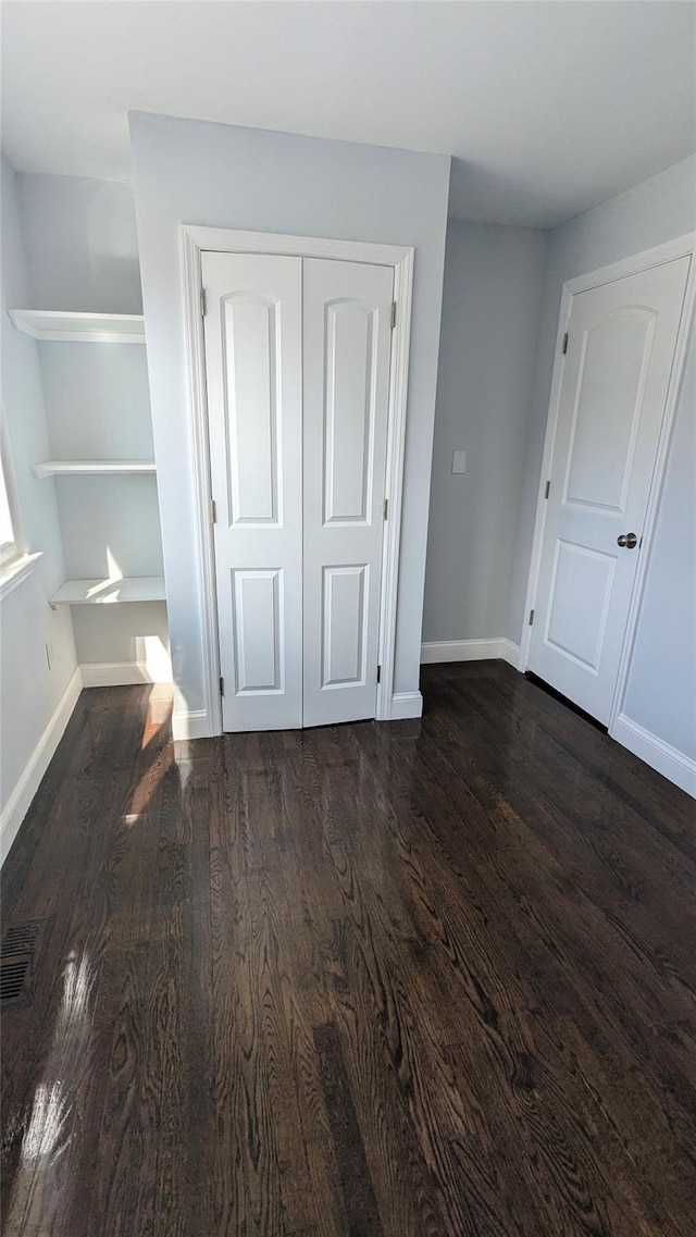 unfurnished bedroom featuring baseboards, visible vents, dark wood finished floors, and a closet