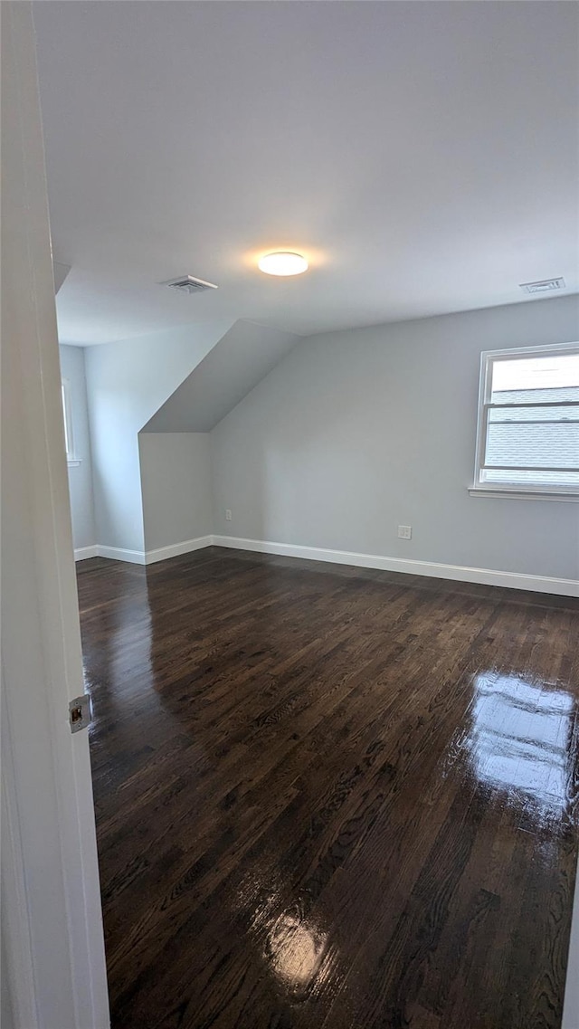 additional living space with dark wood-style flooring, visible vents, vaulted ceiling, and baseboards