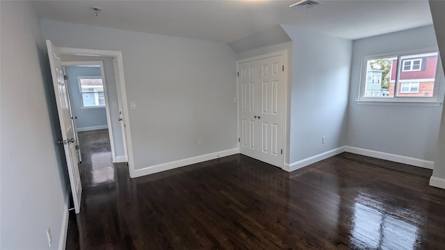 unfurnished bedroom with dark wood-type flooring, a closet, visible vents, and baseboards