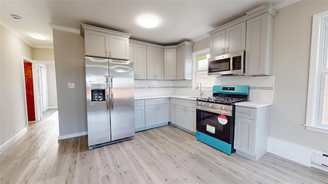 kitchen featuring light wood finished floors, tasteful backsplash, light countertops, appliances with stainless steel finishes, and a sink