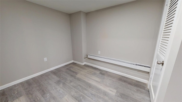 spare room featuring a baseboard radiator, light wood finished floors, and baseboards