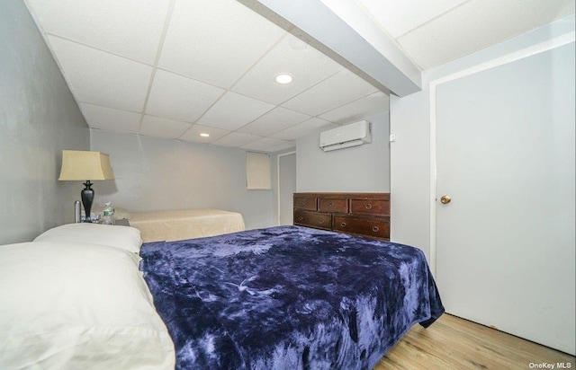 bedroom with a paneled ceiling, wood finished floors, and a wall mounted AC