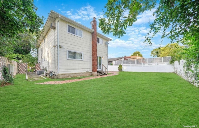 rear view of property with entry steps, a fenced backyard, a chimney, and a yard