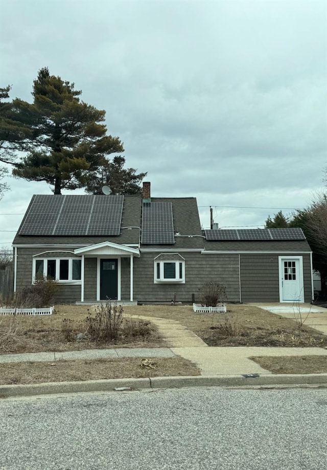 view of front of home featuring roof with shingles, a chimney, and roof mounted solar panels