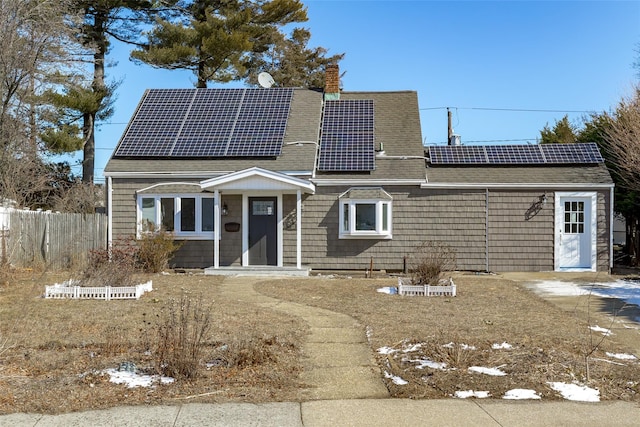 view of front of house featuring roof with shingles, fence, a chimney, and solar panels