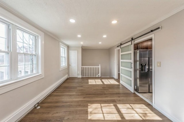 unfurnished room with ornamental molding, a barn door, wood finished floors, and baseboards