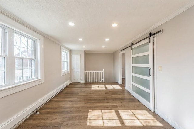 empty room with wood finished floors, crown molding, baseboards, and a barn door