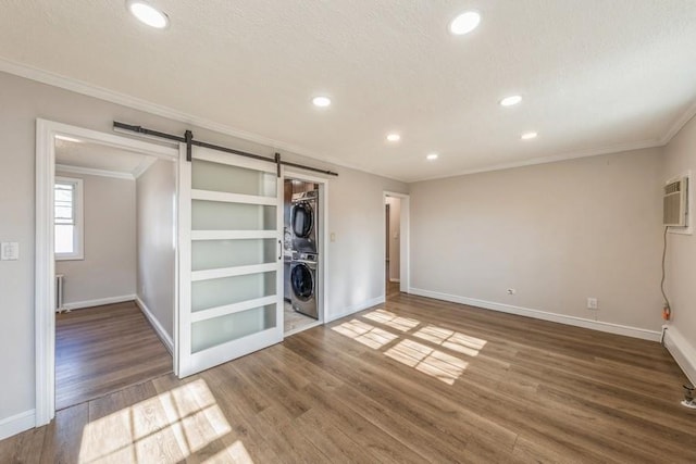 empty room featuring stacked washer and dryer, a barn door, ornamental molding, and wood finished floors