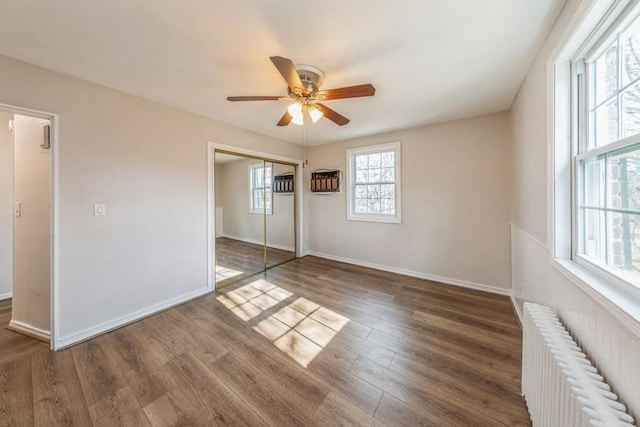 unfurnished bedroom with dark wood-style flooring, radiator heating unit, a closet, and baseboards