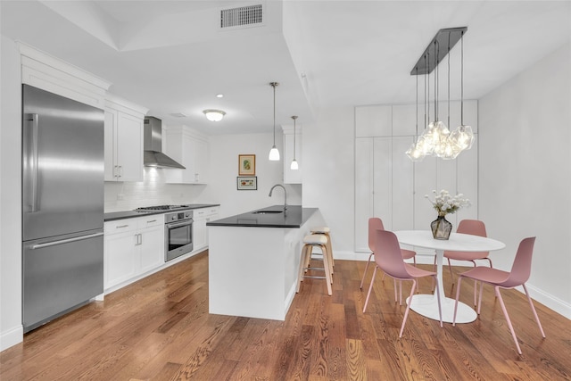 kitchen with visible vents, dark countertops, dark wood-type flooring, stainless steel appliances, and wall chimney range hood