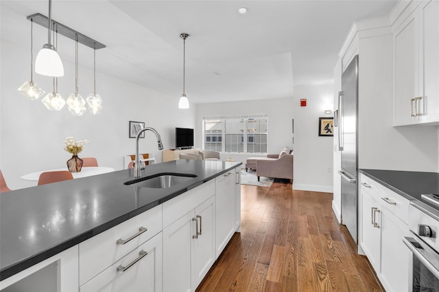 kitchen featuring stainless steel appliances, a sink, white cabinetry, dark countertops, and dark wood finished floors