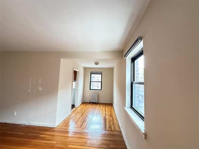 unfurnished room with radiator heating unit, light wood-type flooring, and baseboards